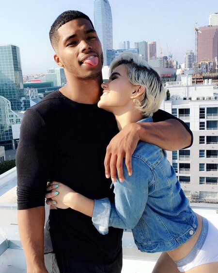 Rome Flynn posing with his tongue out holding Camia Marie. Camia embraces Rome resting her head on Rome's shoulder.