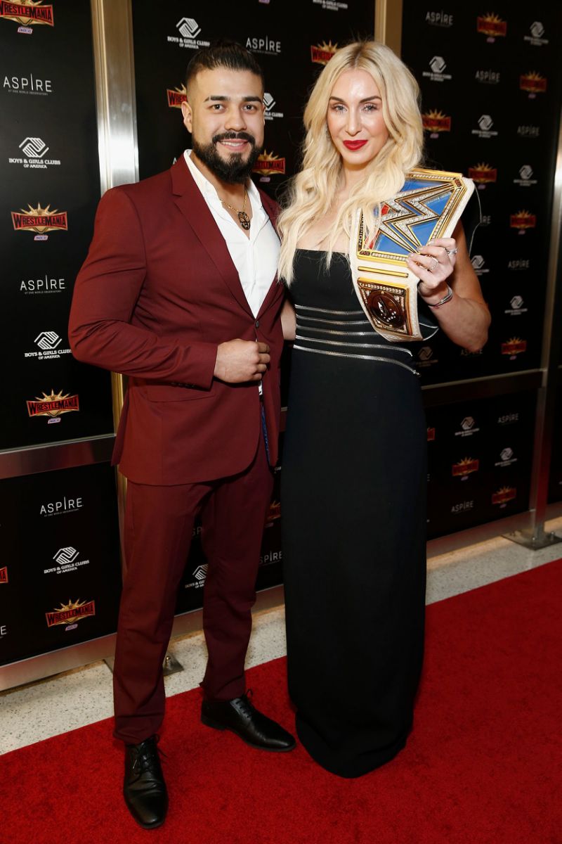andreda in a maroon suit, charlotte in a black gown holding a wrestling belt award