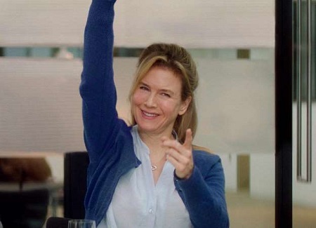 Renée Zellweger raising her one hand and pointing the index finger of the other hand at the camera.