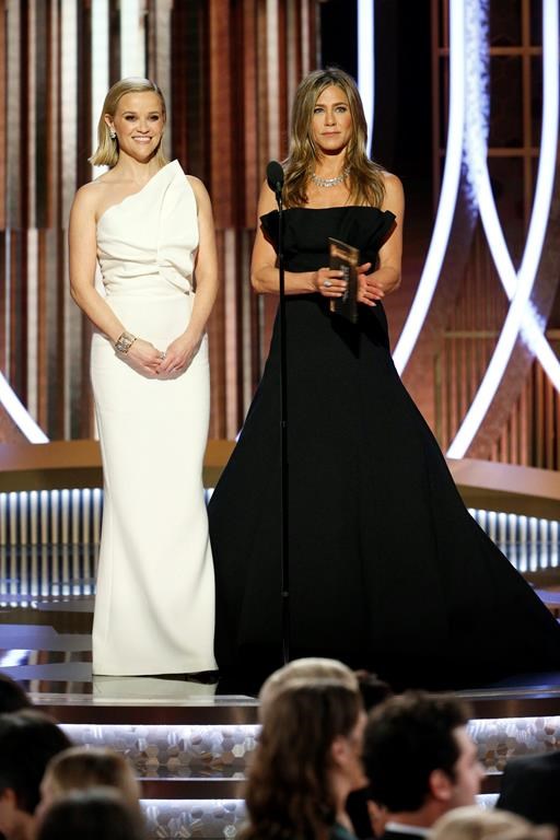 reese and jennifer standing on the stage of golden globe. jennifer wearing strapless black full length gown and reese wearing a one shoulder white gown